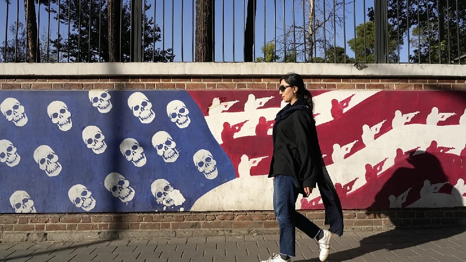 امرأة إيرانية تمر أمام صورة ساخرة للعلم الأمريكي على جدار السفارة الأمريكية السابقة في طهران، إيران، الثلاثاء 22 أكتوبر 2024.