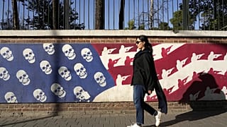 امرأة إيرانية تمر أمام صورة ساخرة للعلم الأمريكي على جدار السفارة الأمريكية السابقة في طهران، إيران، الثلاثاء 22 أكتوبر 2024.