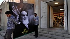رجلان يحملان لافتة عليها صورة مؤسس الثورة الإيرانية الراحل آية الله الخميني عند مدخل السفارة الأمريكية السابقة التي تحولت إلى متحف مناهض لأمريكا في طهران