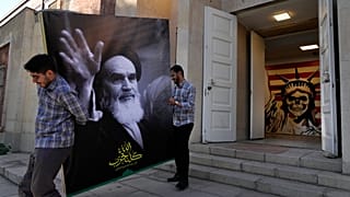 رجلان يحملان لافتة عليها صورة مؤسس الثورة الإيرانية الراحل آية الله الخميني عند مدخل السفارة الأمريكية السابقة التي تحولت إلى متحف مناهض لأمريكا في طهران
