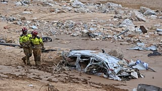 Kurtarma görevlileri, 3 Kasım 2024 Pazar günü İspanya'nın Valensiya kenti yakınlarındaki Paiporta'da meydana gelen sel felaketinin ardından yarıya kadar gömülmüş bir arabanın yanından geçiyor.