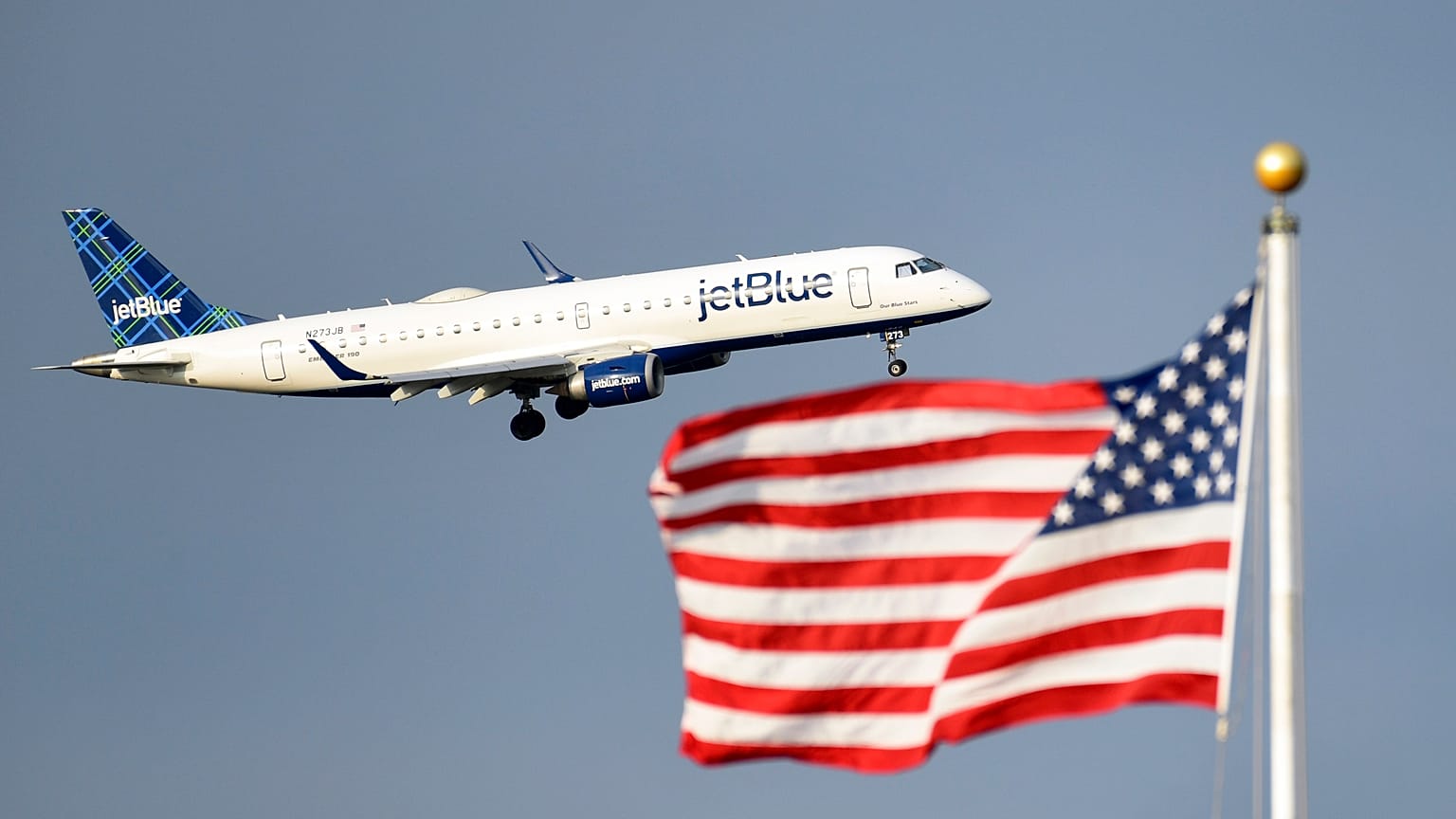 Um jato de passageiros da JetBlue passa junto à bandeira dos EUA.