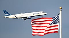 Ένα επιβατικό αεροσκάφος της JetBlue πετάει μπροστά από τη σημαία των ΗΠΑ.