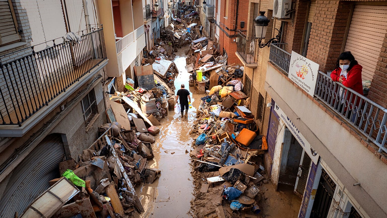 Gente camina por una calle con muebles amontonados y basura a los lados en una zona, afectada por las inundaciones, en Paiporta, Valencia, España, el martes 5 de noviembre de 2024. 