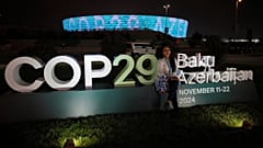 A woman poses for a photo with the Baku Olympic Stadium in the background as it is illuminated at COP29.