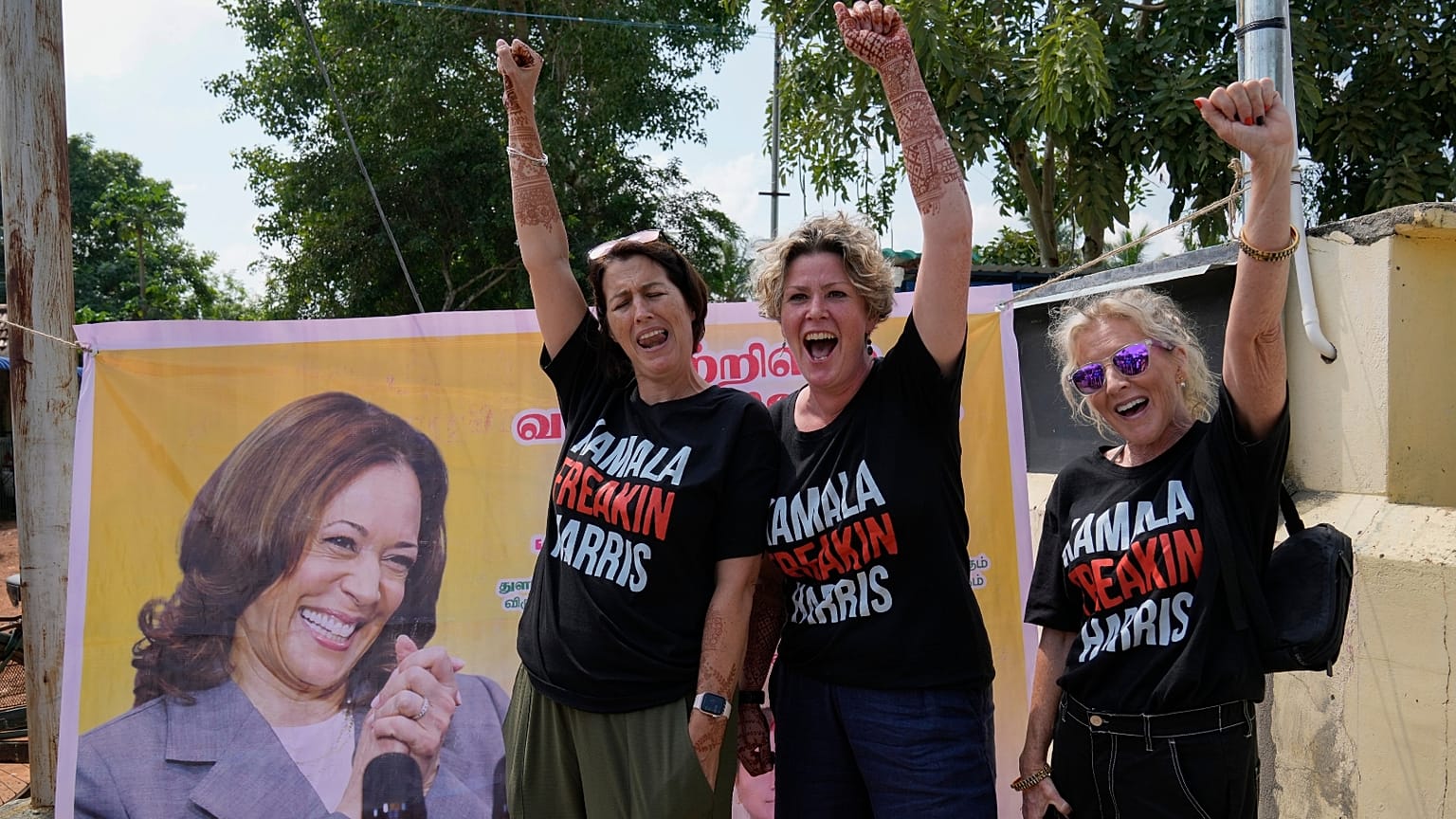 Três mulheres aplaudem a candidata democrata à presidência, a vice-presidente Kamala Harris, à porta de um templo em Thulasendrapuram, a aldeia ancestral de Harris, na Índia