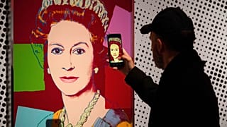 Un hombre fotografía una serigrafía de Andy Warhol de la reina Isabel II, parte de la serie "Reigning Queens" de 1985, en el museo Paleis Het Loo de Apeldoorn (Países Bajos).