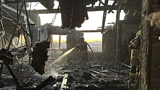 Bir itfaiyeci Rus saldırılarında yıkılan bir binanın kalıntılarını hortumla yıkıyor.