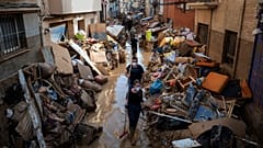 Pessoas caminham por uma rua com mobiliário empilhado e lixo nas bermas, numa zona afetada pelas inundações, em Paiporta, Valência, Espanha.