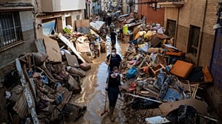 Pessoas caminham por uma rua com mobiliário empilhado e lixo nas bermas, numa zona afetada pelas inundações, em Paiporta, Valência, Espanha.