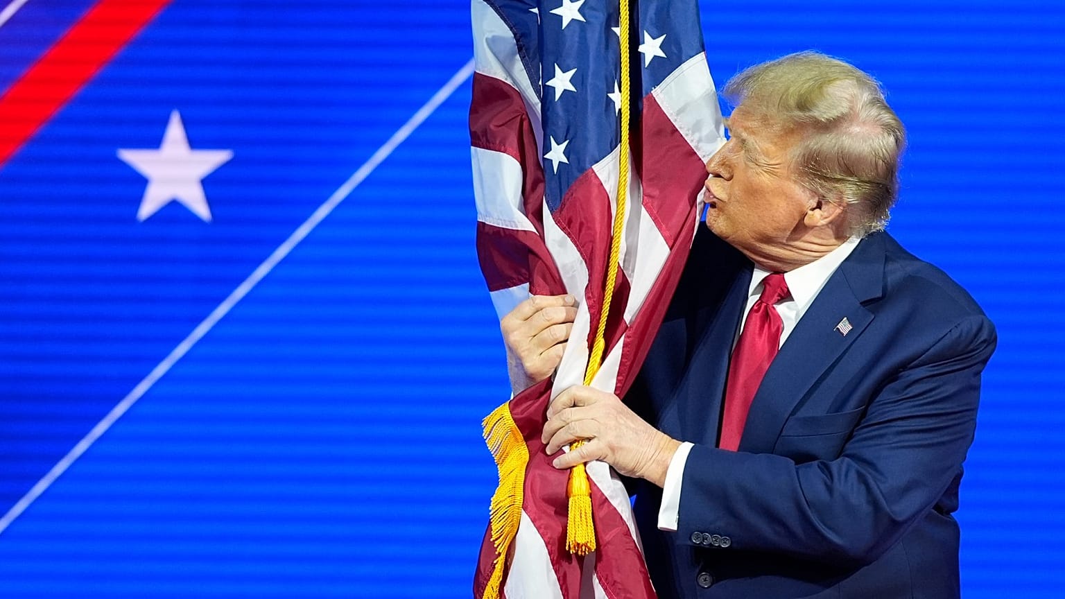 Donald Trump abraça e beija a bandeira americana enquanto discursa na Conferência de Ação Política Conservadora, em fevereiro de 2024.