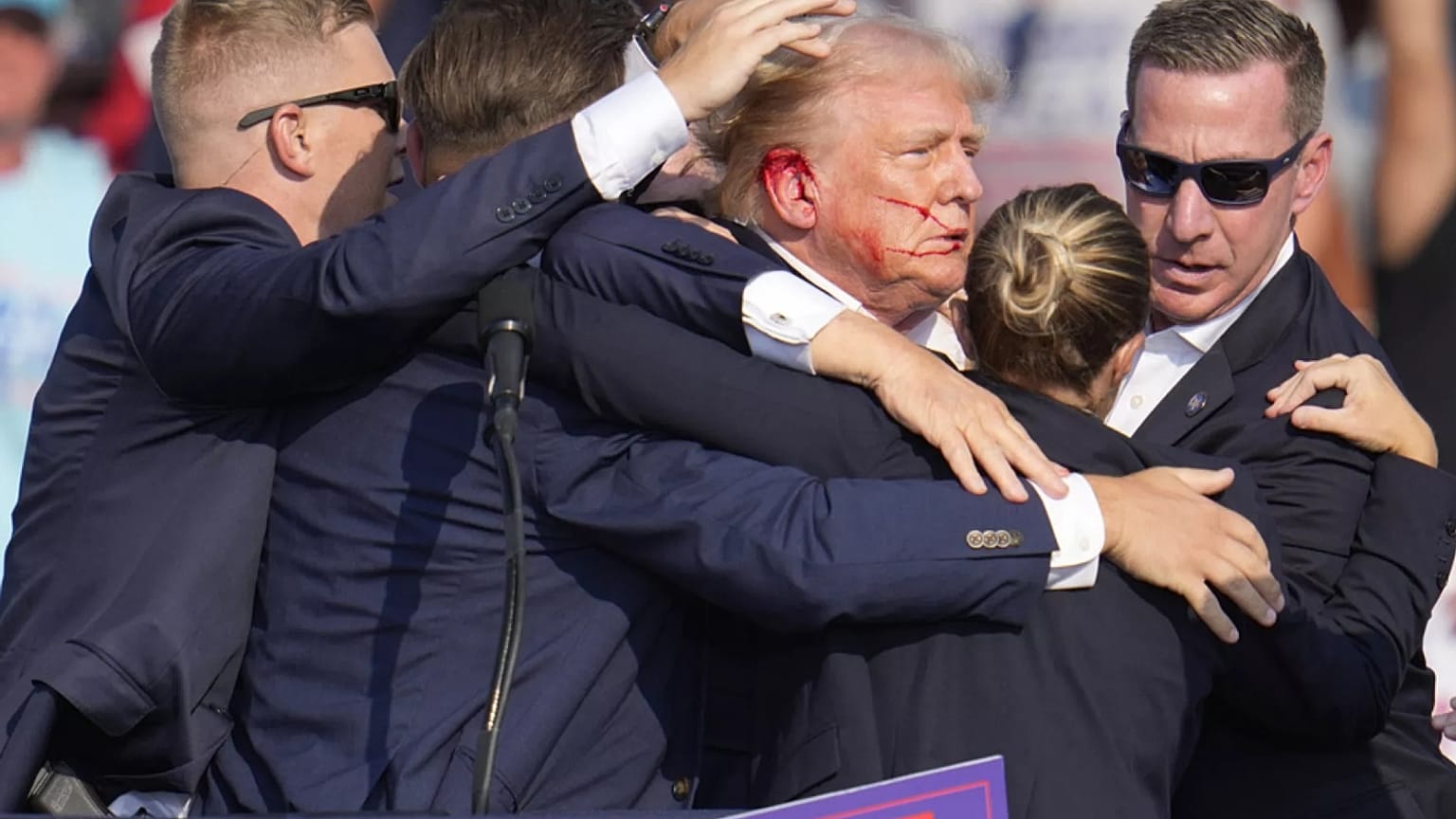 الدماء على أذن ترامب بعد إصابته في محاولة اغتيال في تموز/ يوليو الماضي، وعناصر جهاز الخدمة السرية يحيطون به. 