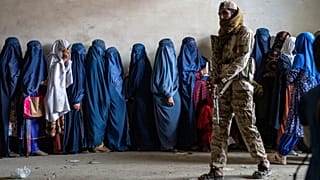یک نیروی طالبان در کنار صف زنان برای دریافت جیره غذایی در کابل افغانستان، در ۲۳ مه ۲۰۲۳
