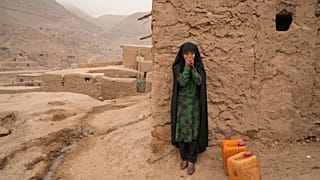 DOSYA - 14 Aralık 2021, Pazartesi günü Afganistan'ın Balucha kentinde su taşırken dinlenen Afgan bir kız ellerini ısıtıyor. (AP Fotoğrafı/Mstyslav Chernov, Dosya)