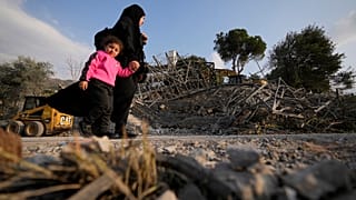 Egy Izrael által lebombázott ház mellett halad egy nő és gyermeke Libanonban