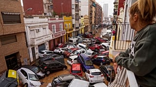 A woman looks out from her balcony as vehicles are trapped in the street during flooding in Valencia.