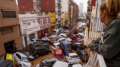 A woman looks out from her balcony as vehicles are trapped in the street during flooding in Valencia.