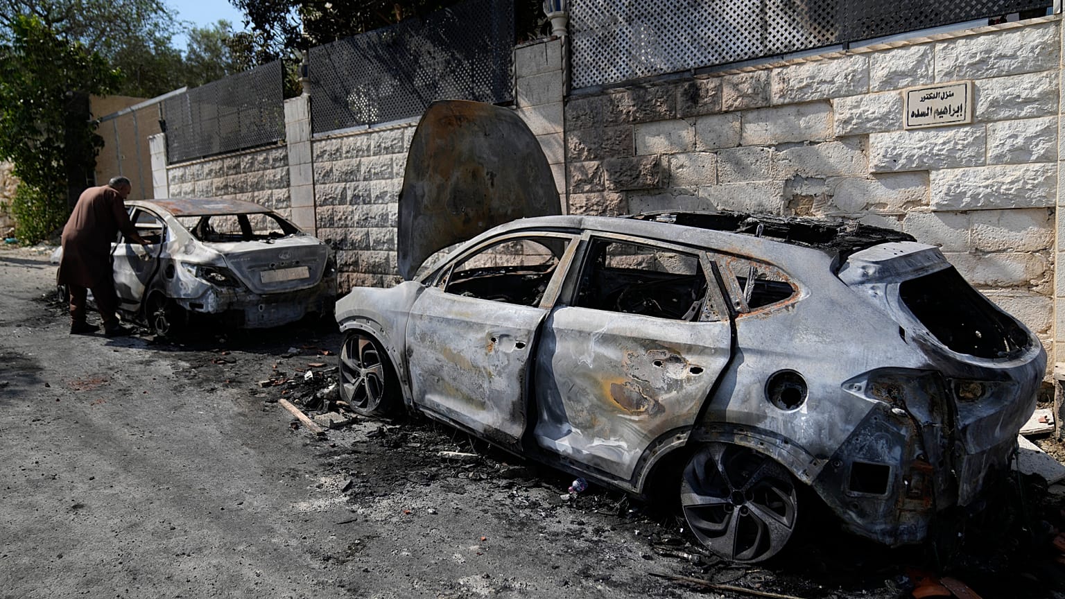 فلسطيني يتفحص سيارة محترقة شوهدت صباح يوم الجمعة 16 أغسطس/آب 2024، بعد هجوم شنه مستوطنون إسرائيليون في قرية جيت بالضفة الغربية