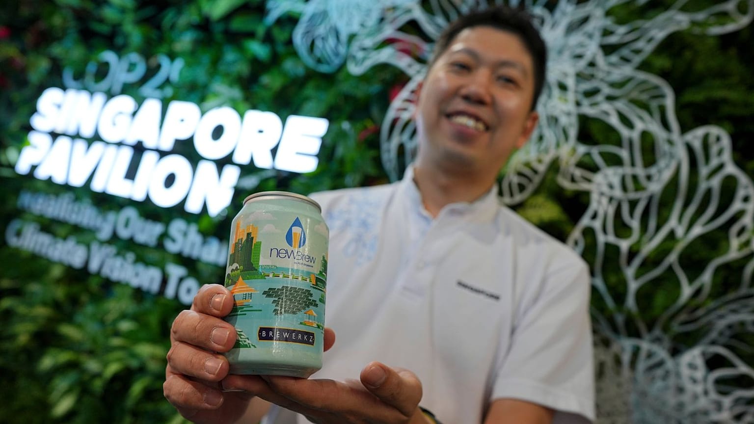 COP29 Singapur Pavilyonu ekibinden Nick Chow, arıtılmış atık su ile yapılan NEWBrew birası ile poz veriyor.