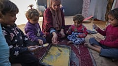 عائلة فلسطينية تجتمع حول طبق من البرغل وتشاركه في ظل نقص الإمدادات الغذائية والمجاعة التي تهدد غزة.