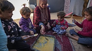 عائلة فلسطينية تجتمع حول طبق من البرغل وتشاركه في ظل نقص الإمدادات الغذائية والمجاعة التي تهدد غزة.