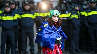 Una donna avvolta in una bandiera dell'Ue davanti alla polizia che blocca l'ingresso dell'edificio del Parlamento a Tbilisi, Georgia, 25 novembre 2024