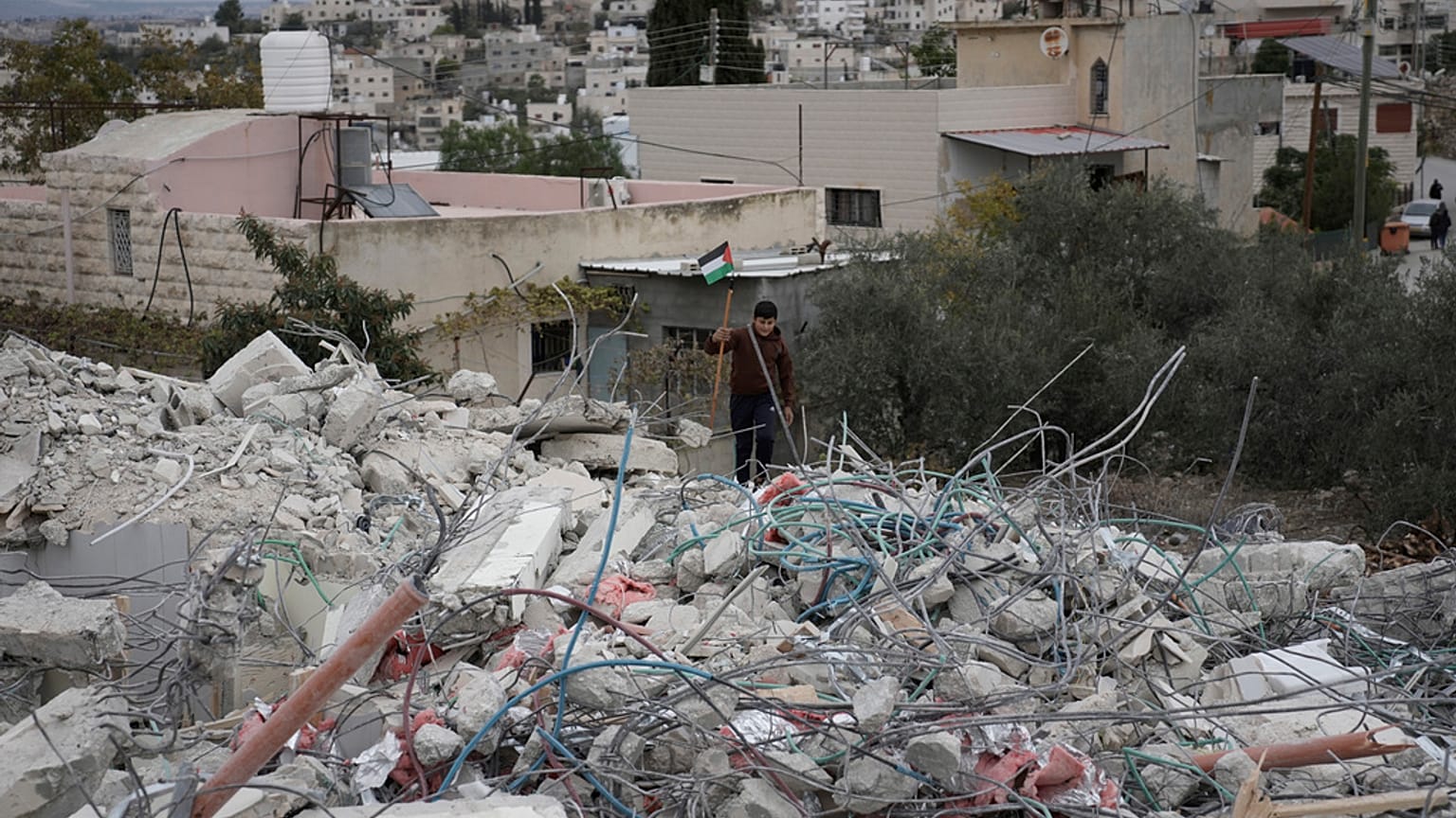 طفل يحمل العلم الفلسطيني فوق الدمار الذي أحدثته الحرب على غزة