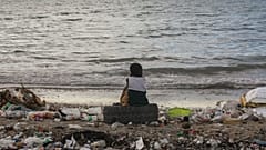 A boy sits on a tire among garbage during sunset at a beach in Saint-Marc, Haiti.
