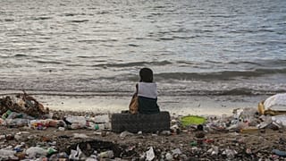 A boy sits on a tire among garbage during sunset at a beach in Saint-Marc, Haiti.