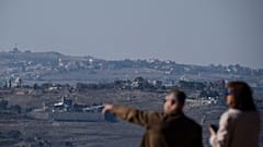 زوجان إسرائيليان يراقبان المباني المتضررة في قرية بجنوب لبنان أثناء وقوفهما بالقرب من الحدود الإسرائيلية اللبنانية