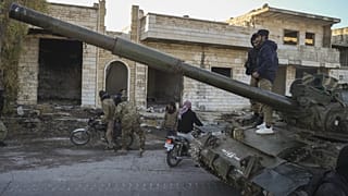 Muhalif militanların destekçileri, Suriye'nin Halep kentinin güneybatısındaki Maaret el-Numan kasabasında ordunun ele geçirilen zırhlı aracının üzerinde duruyor