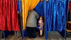 Ана Каролина, 3,5 года, стоит в кабинке для голосования, пока мужчина голосует на парламентских выборах в Бухаресте, Румыния, воскресенье, 1 декабря 2024 года.