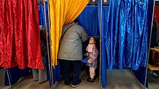 Η Ana Caroline, 3,5 ετών, στέκεται σε μια κάλπη καθώς ένας άνδρας ψηφίζει στις βουλευτικές εκλογές της χώρας, στο Βουκουρέστι της Ρουμανίας, Κυριακή 1 Δεκεμβρίου 2024.