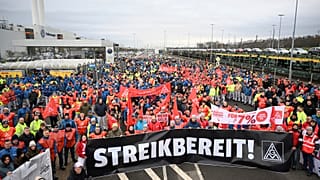 Volkswagen-Beschäftigte schwenken Gewerkschaftsfahnen, als sie am ersten Tag eines bundesweiten Warnstreiks vor einem VW-Werk in Zwickau demonstrieren