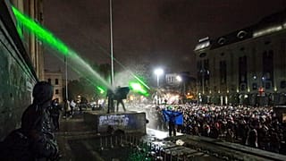 Göstericiler 2 Aralık 2024 Pazartesi günü Gürcistan'ın başkenti Tiflis'te parlamentonun önünde tazyikli su altında bir mezarın üzerinde duruyor.