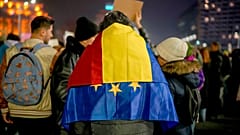A man with the Romanian and European Union flags on his shoulders takes part in a protest against Calin Georgescu, 27 November 2024