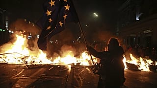 Un manifestant tient un drapeau de l'Union européenne à côté d'une barricade en feu lors d'un rassemblement à Tbilissi, en Géorgie, tôt le mardi 3 décembre