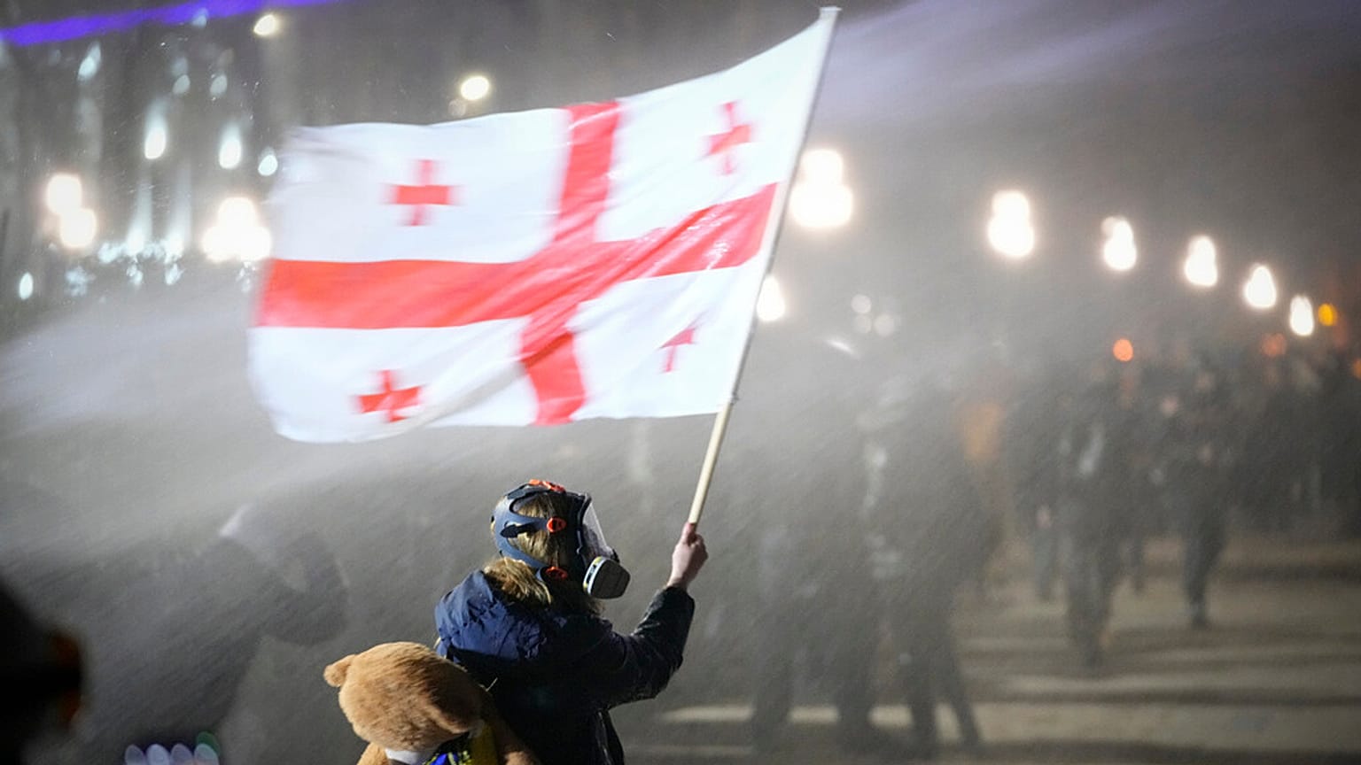 Demonstrant trzyma gruzińską flagę narodową, gdy jest spryskiwany armatką wodną przed parlamentem podczas protestu w Tbilisi w Gruzji, na początku wtorku, 3 grudnia 2024 r.