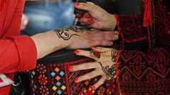 امرأة تقوم برسم الحناء على يد متسابقة فلسطينية قبل مشاركتها في مسابقة الجمال وتصفيف الشعر في مهرجان في مدينة طولكرم بالضفة الغربية، الإثنين، 12 مايو، 2014.