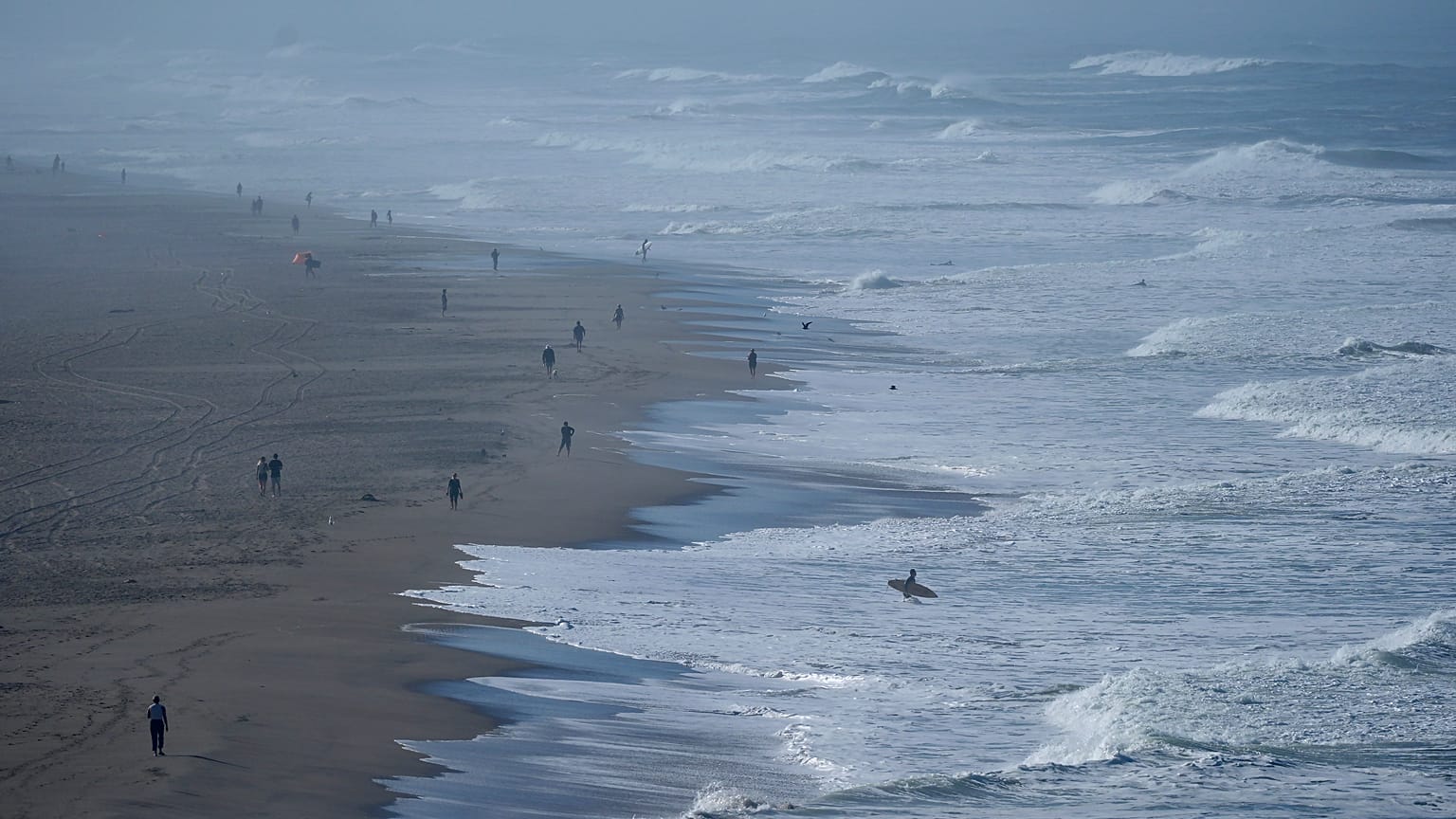 Un surfista camina hacia el agua mientras la gente visita Ocean Beach en San Francisco, el jueves 3 de octubre de 2024.