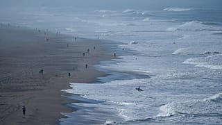 Un surfista camina hacia el agua mientras la gente visita Ocean Beach en San Francisco, el jueves 3 de octubre de 2024.