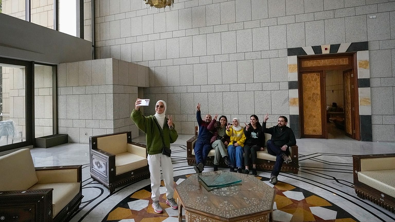 Um grupo de pessoas tira uma fotografia de família numa sala do palácio presidencial do presidente sírio Bashar al-Assad em Damasco, Síria, 8.12.2024