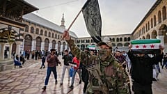 Maskeli bir muhalif savaşçı, Şam kentindeki Emevi Camii'nin avlusunda Hayat Tahrir Şam (HTŞ) bayrağı taşıyor, 10 Aralık 2024.