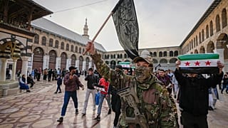 Maskeli bir muhalif savaşçı, Şam kentindeki Emevi Camii'nin avlusunda Hayat Tahrir Şam (HTŞ) bayrağı taşıyor, 10 Aralık 2024.