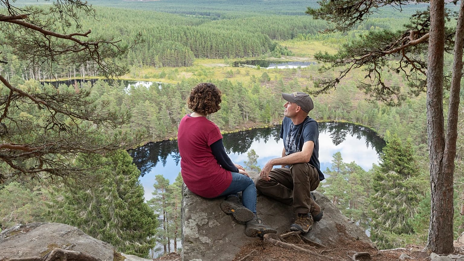 A couple sit and look out across Uath Lochans in Cairngorms National Park, Scotland 