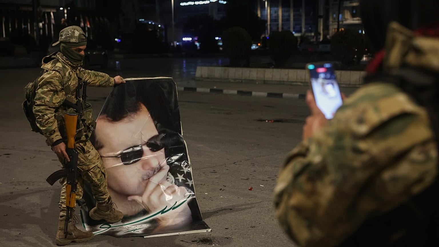 Un combatiente de la oposición siria hace una foto a un compañero que pisa un retrato del derrocado presidente sirio Bashar Assad en Alepo.