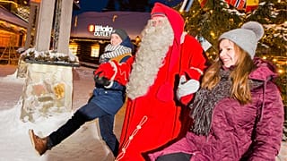 Laponya'daki Noel Baba Köyü'nde Noel Baba kostümü giymiş bir kişi, iki kişinin elini tutuyor