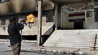 Bir muhalif militan, Suriye'de girişinde Beşar ve Hafız Esad'ın posterinin yer aldığı gözaltı merkezinin girişine ateş açıyor