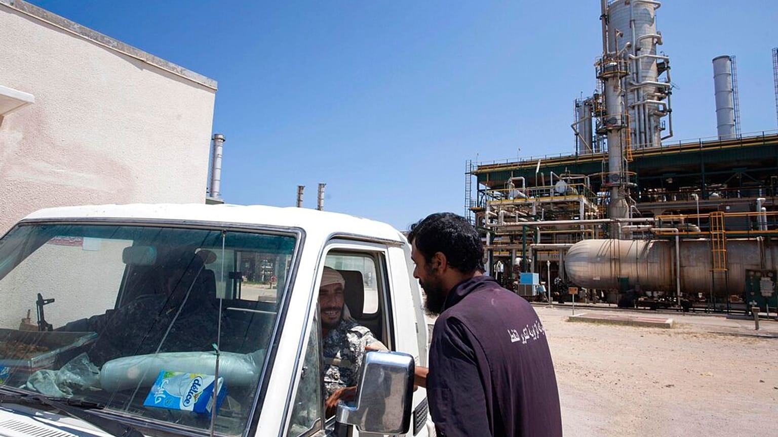 DOSSIER - Un ouvrier libyen discute avec deux rebelles qui patrouillent dans une raffinerie de pétrole contrôlée par les forces anti-Kadhafi dans la banlieue ouest de Zawiya, le 19 août 2011.