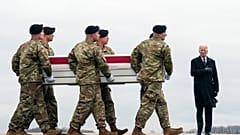 El presidente Joe Biden, a la derecha, de pie mientras un equipo de transporte del Ejército.